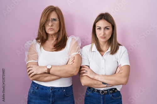Hispanic mother and daughter wearing casual white t shirt over pink background skeptic and nervous, disapproving expression on face with crossed arms. negative person.