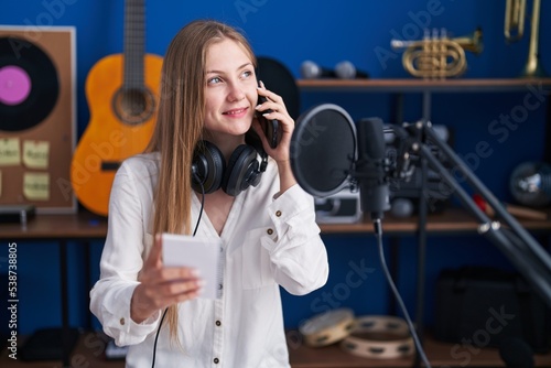 Young caucasian woman artist talking on smartphone reading notebook at music studio