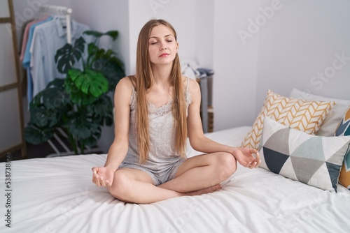 Young caucasian woman doing yoga exercise sitting on bed at bedroom