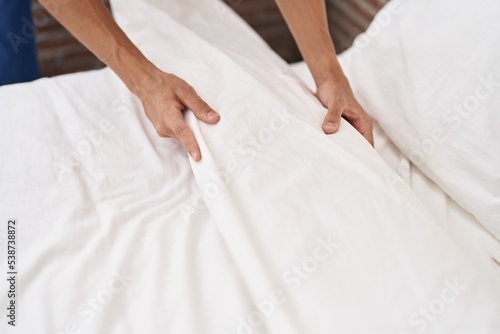 Young hispanic man make bed at bedroom