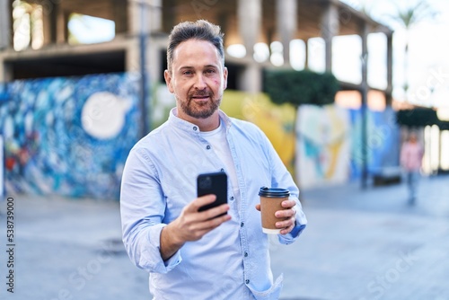 Young caucasian man using smartphone drinking coffee at street