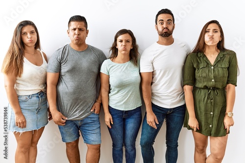 Fényképezés Group of young hispanic friends standing together over isolated background puffing cheeks with funny face