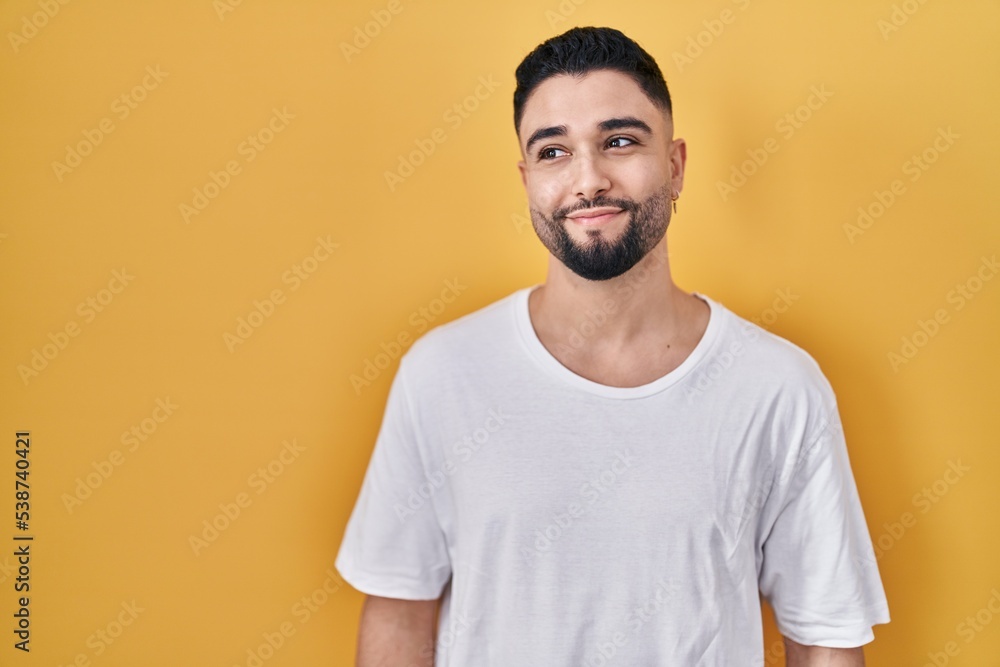 Young handsome man wearing casual t shirt over yellow background smiling looking to the side and staring away thinking. Young handsome man wearing casual t shirt over yellow background smiling looking to the side and staring away thinking.