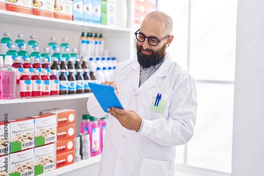 Young bald man pharmacist using touchpad working at pharmacy