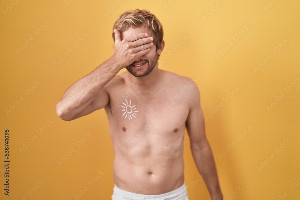 Caucasian man standing shirtless wearing sun screen smiling and laughing with hand on face covering eyes for surprise. blind concept.