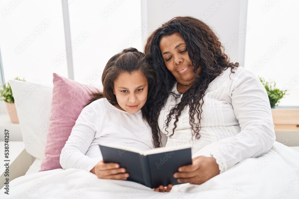 Mother and daughter reading book sitting on bed at bedroom Mother and daughter reading book sitting on bed at bedroom