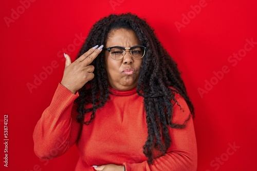 Plus size hispanic woman standing over red background shooting and killing oneself pointing hand and fingers to head like gun, suicide gesture.