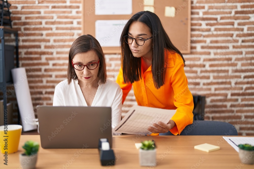 Two women business workers using laptop reading document at office Two women business workers using laptop reading document at office