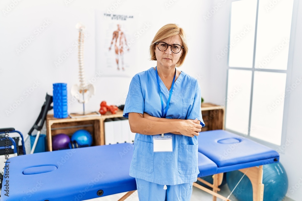 Middle age blonde woman working at pain recovery clinic skeptic and nervous, disapproving expression on face with crossed arms. negative person. Middle age blonde woman working at pain recovery clinic skeptic and nervous, disapproving expression on face with crossed arms. negative person.