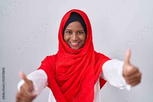 Young arab woman wearing traditional islamic hijab scarf approving doing positive gesture with hand  thumbs up smiling and happy for success. winner gesture.