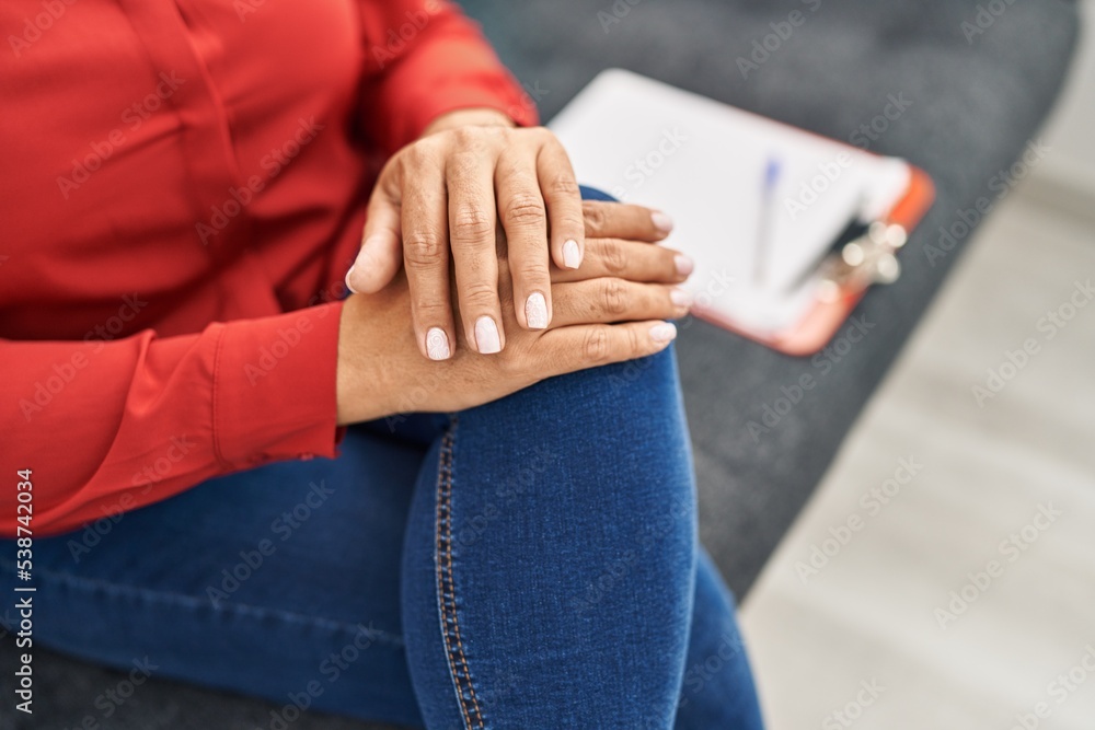 Middle age hispanic woman psychologist sitting on sofa at psychology center