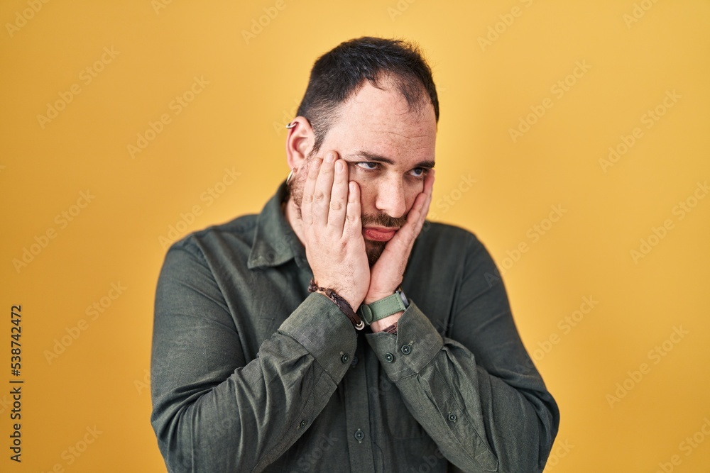 Plus size hispanic man with beard standing over yellow background tired hands covering face, depression and sadness, upset and irritated for problem Plus size hispanic man with beard standing over yellow background tired hands covering face, depression and sadness, upset and irritated for problem