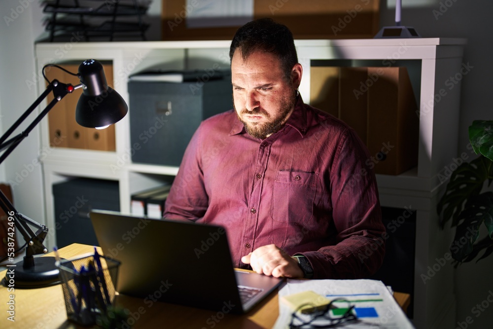 Plus size hispanic man with beard working at the office at night puffing cheeks with funny face. mouth inflated with air, crazy expression. Plus size hispanic man with beard working at the office at night puffing cheeks with funny face. mouth inflated with air, crazy expression.