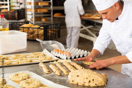 Concentrated baker preparing sweet buns in bakery kitchen