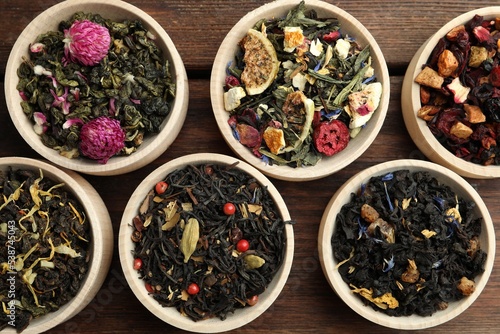 Different kinds of dry herbal tea in bowls on wooden table  flat lay