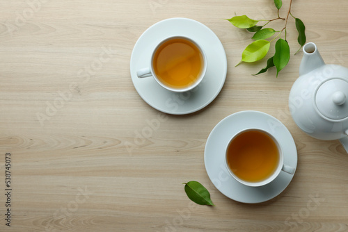 Green tea in white cups with leaves and teapot on wooden table  flat lay. Space for text