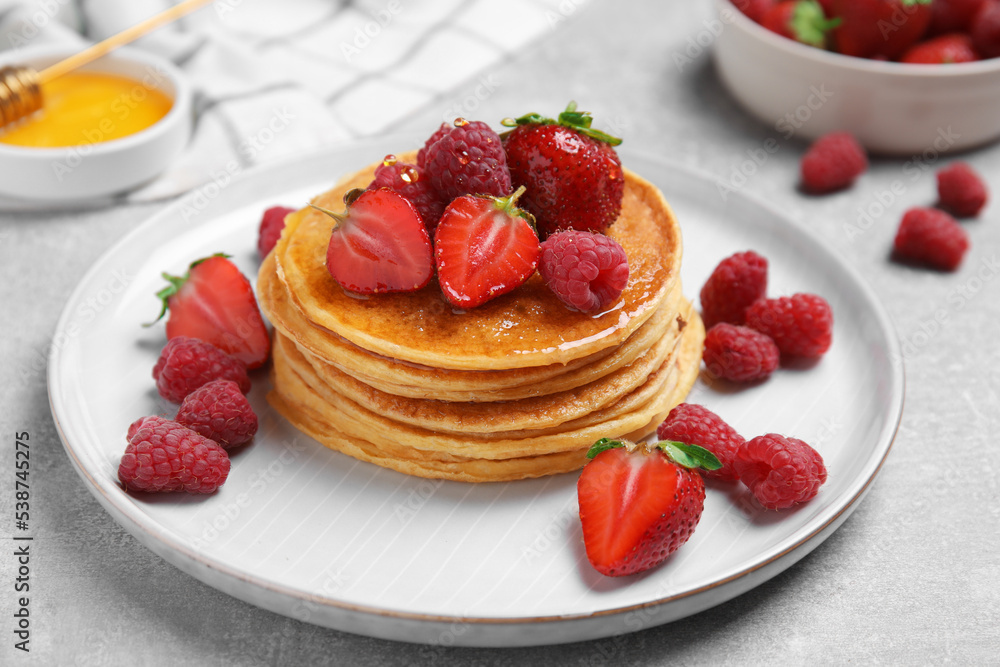 Tasty pancakes with fresh berries and honey on light grey table, closeup Tasty pancakes with fresh berries and honey on light grey table, closeup