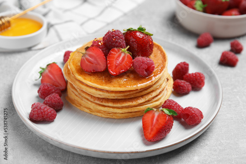 Tasty pancakes with fresh berries and honey on light grey table, closeup