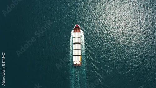 Aerial top down view: Freight ship full of containers sailing in open sea. Huge marine craft shipping import export cargo transport. Commercial business logistic