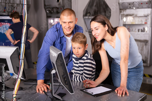 Cheerful young parents with two sons spending funny time in quest room decorated as lost underground shelter using computer to find solution to puzzle