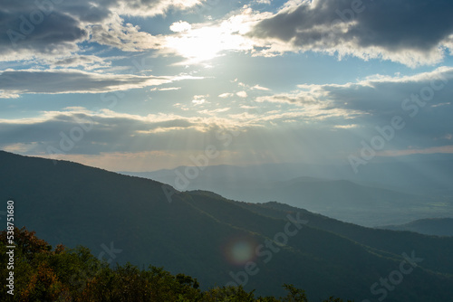 Rays of light shine down from a cloudy but blue sky onto the sides of the Blue Ridge Mountains as seen from Skyline Drive inside Shenandoah National Park, Virginia.