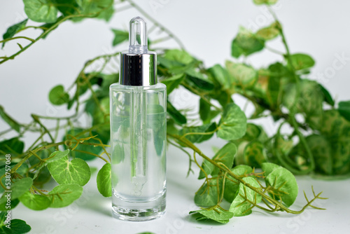 A perfume or essential oil glass bottle on a white background surrounded by green leafs