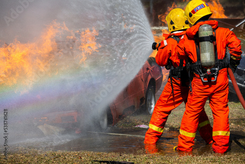 Asian firefighter on duty firefighting, Asian fireman spraying high pressure water, Fireman in fire fighting equipment uniform spray water from hose for fire fighting.