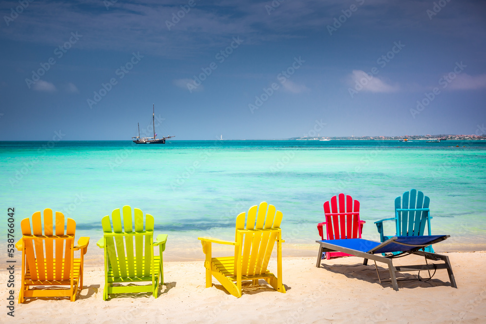 Colorful chairs in Aruba, turquoise caribbean beach with ship, Dutch Antilles