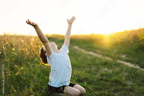 Boy closed her eyes and praying in a field at sunset. Hands folded in prayer concept for faith, spirituality and religion.