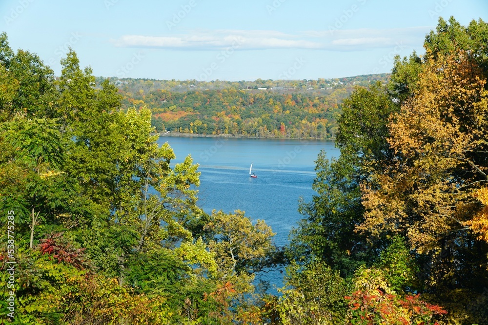 A distance view of a sailboat with the background of fall foliage near Cayuga Lake, New York
