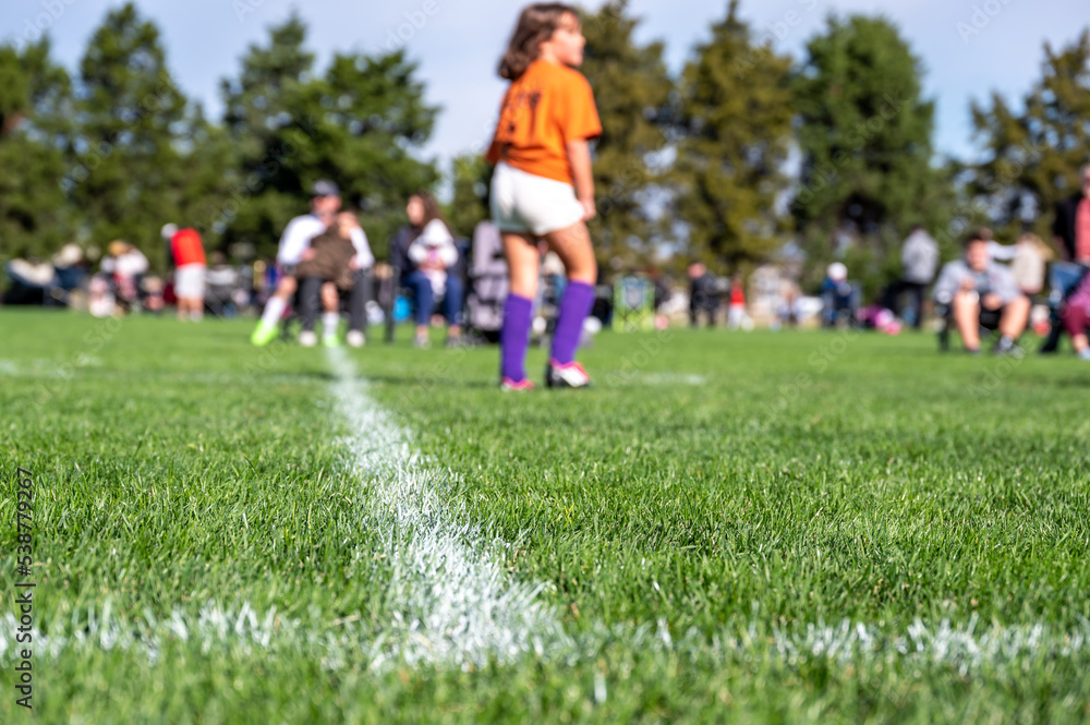 Obraz premium Selective focus on ground level view of soccer field center line with defocused youth girls in background