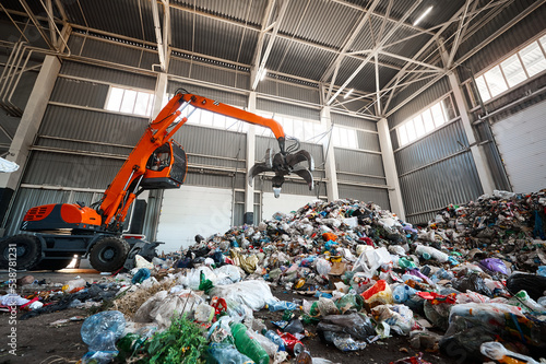 Obraz na plátně Grabbing excavator collects garbage in plant warehouse