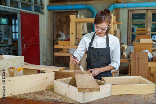 portrait of beautiful asian woman carpenter dealing with handicraft, woman has own business connected with making wooden furniture in workshop