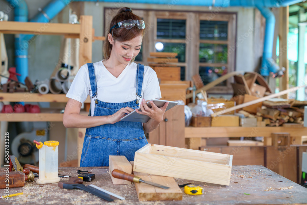 portrait of beautiful asian woman carpenter dealing with handicraft, woman has own business connected with making wooden furniture in workshop.