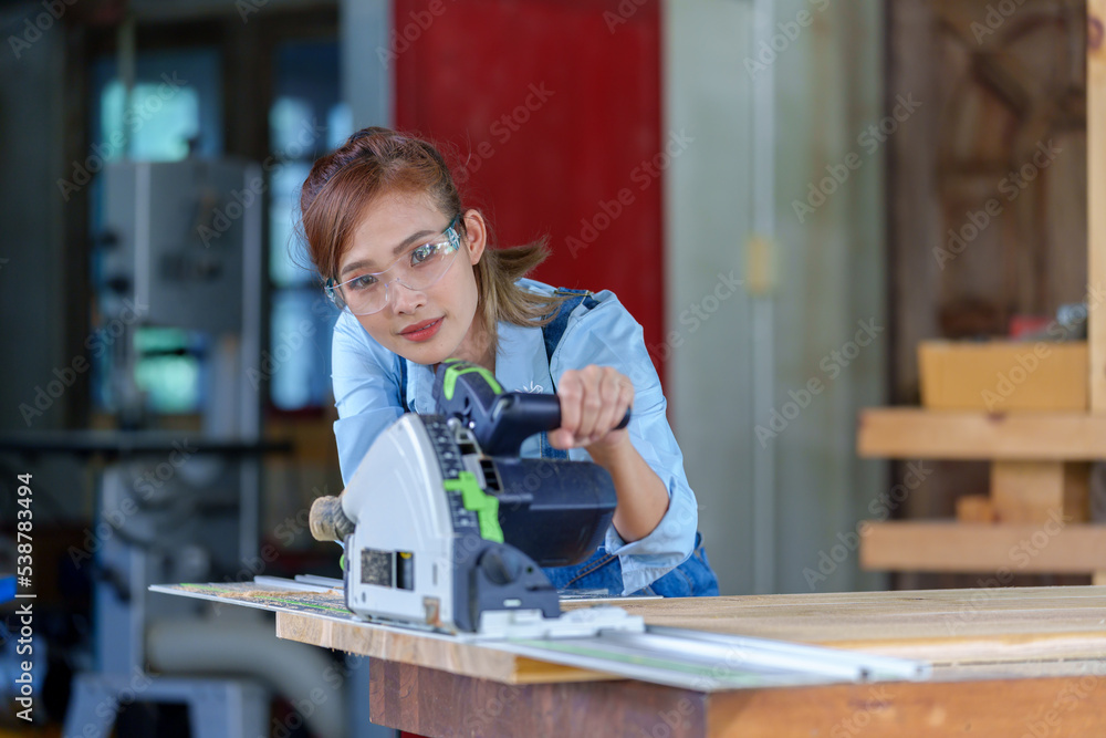 Female Carpentry Student In Workshop Studying For Apprenticeship At College Using Bench Saw Female Carpentry Student In Workshop Studying For Apprenticeship At College Using Bench Saw