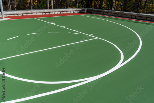 Interesting green and red outdoor basketball court at school playground. Court includes retaining walls and black vinyl coated chain link fence. 