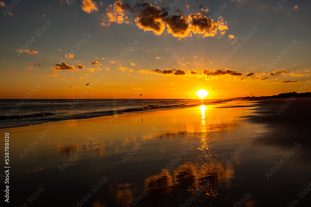 Incredible sunset on the beach. Reflections of the golden lights in the water on the beach.
