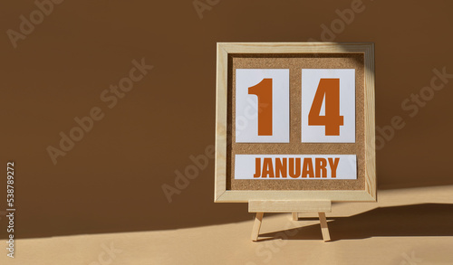 January 14th. Day 14 of month, Calendar date. Cork board, easel in sunlight on desktop. Close-up, brown background. Winter month, day of year concept photo