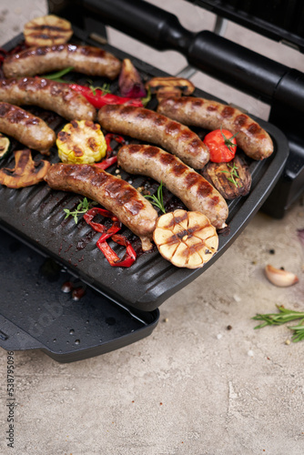 Grilled sausages and vegetables on electric grill at domestic kitchen