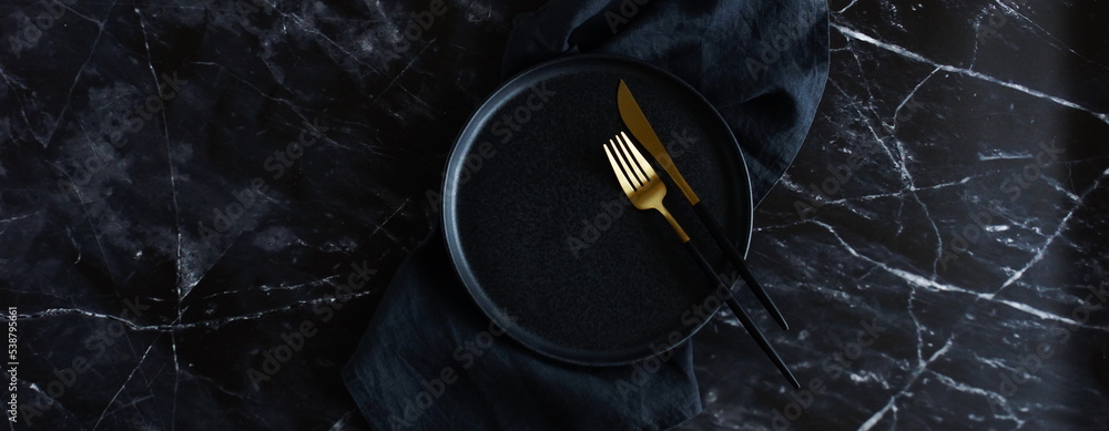 Empty black plate, fork ,knife, linen napkin top view banner. Black kitchen utensils set on black marble  table. Top view flat lay with copy space