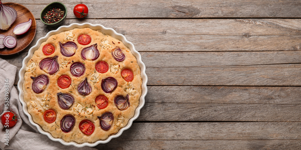 Baking dish with tasty Italian focaccia and ingredients on wooden background with space for text