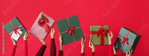 Many hands with Christmas gifts on red background photo