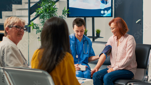 Medical assistant doing cardiac examination with tonometer to measure hypertension and pulse pressure. Nurse using medical instrument to check hypotension in healthcare clinic. photo