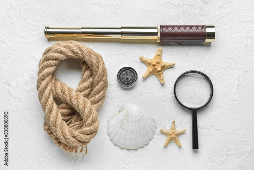 Vintage spyglass, magnifier, compass, starfishes and rope on light background