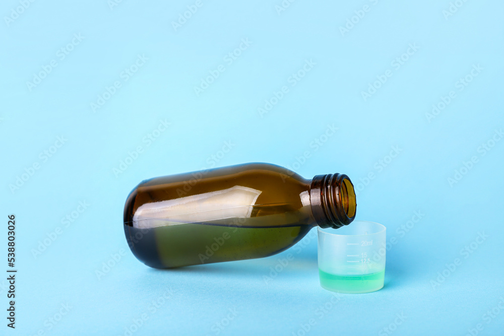 Fototapeta premium Bottle of cough syrup and cup on blue background