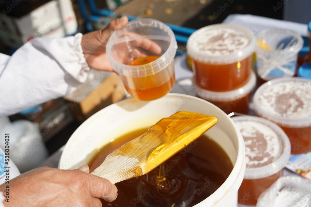 The seller pours fresh honey into a container at the market. The seller pours fresh honey into a container at the market.