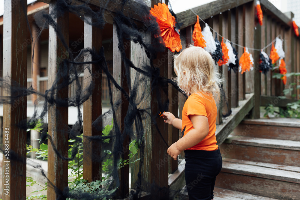 Lifestyle portrait of Happy caucasian baby girl with blonde hair in black orange costume celebrating Halloween outdoor