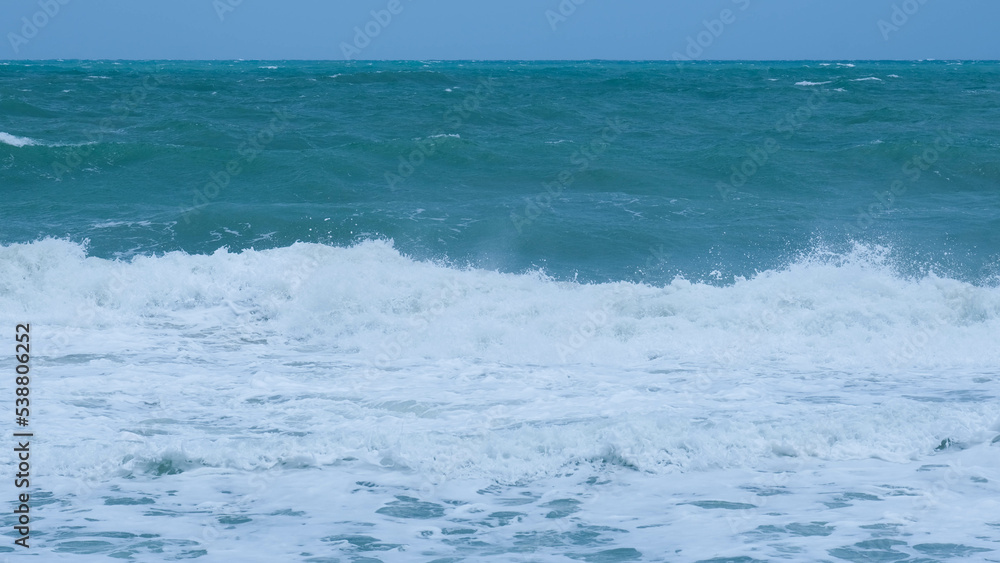 View of sea waves on the beach of tropical seas in Thailand. Strong sea waves crash to shore in the rainy season. Beautiful sea waves with foam of blue and turquoise color. View of sea waves on the beach of tropical seas in Thailand. Strong sea waves crash to shore in the rainy season. Beautiful sea waves with foam of blue and turquoise color.
