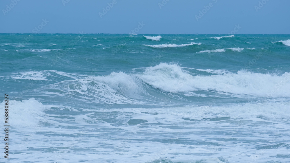 View of sea waves on the beach of tropical seas in Thailand. Strong sea waves crash to shore in the rainy season. Beautiful sea waves with foam of blue and turquoise color.