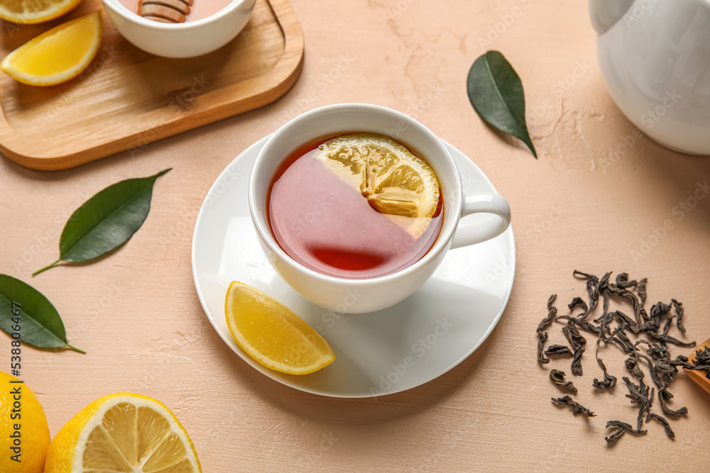 Cup of black tea with lemon and leaves on beige background Cup of black tea with lemon and leaves on beige background